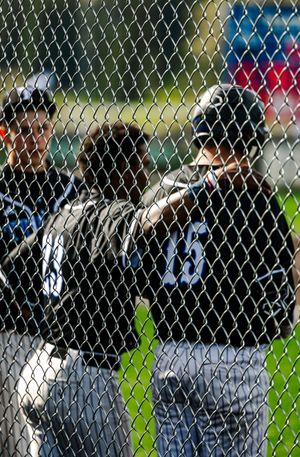 Baseball players in black uniforms standing in dugout behind chain-link fence during a game.