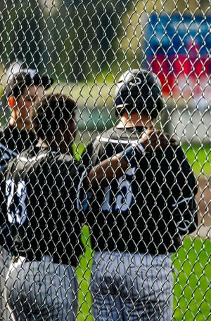 Baseball players in black uniforms huddle behind a chain-link fence dugout during a game.