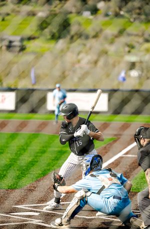 Baseball batter number 15 in black uniform takes swing as catcher and umpire watch closely.
