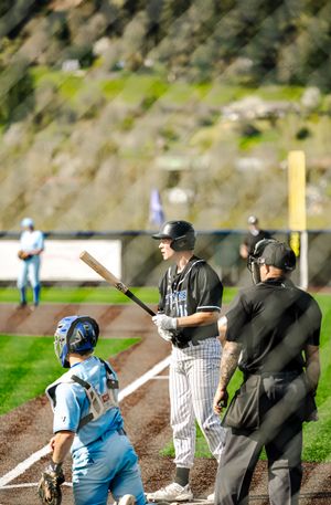 Baseball batter in black pinstripe uniform stands at home plate with catcher and umpire during game.