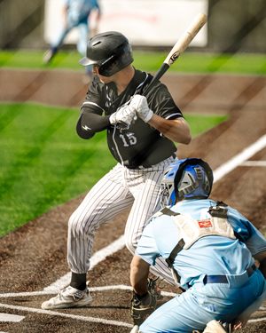 Baseball batter #15 in black pinstripe uniform at home plate with catcher in blue gear behind him.
