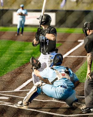 Baseball batter swings while catcher crouches and umpire watches during a game.