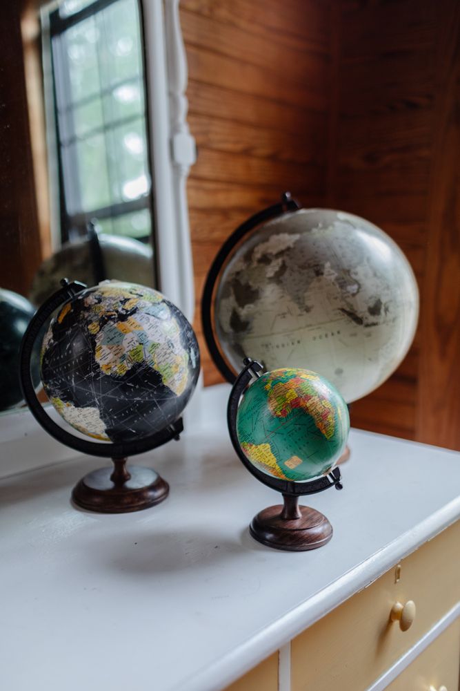 Three antique globes sit on a yellow and white painted dresser in an oak walled bedroom. Lake Winnipesaukee family vacation photographer
