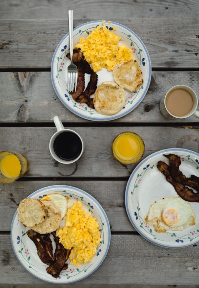 Above view of three plates with scrambled eggs, orange juice, and coffee on a rustic wooden table. Southern Maine family photographer