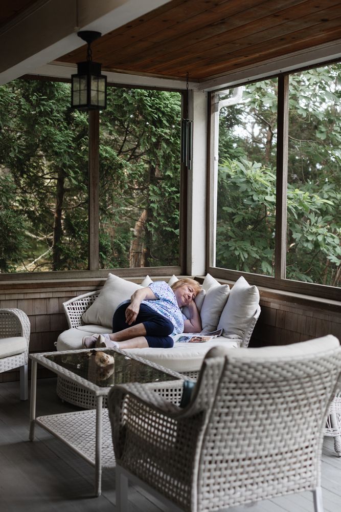 Grandmother naps on a corner chair on a screened porch in cabin. Cape Cod family vacation photographer.