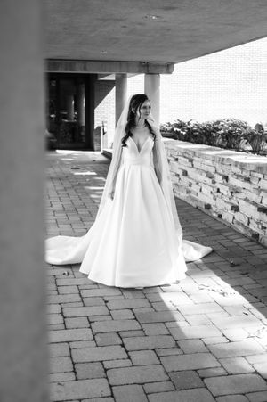 Bride in elegant white ball gown with veil poses on brick patio in black and white wedding portrait.