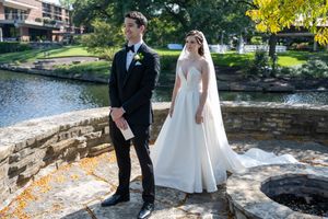 Bride and groom share a first look moment on stone terrace by a river in autumn wedding photos.