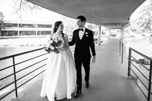 Black and white photo of a bride and groom walking hand in hand along a covered walkway on their wedding day.