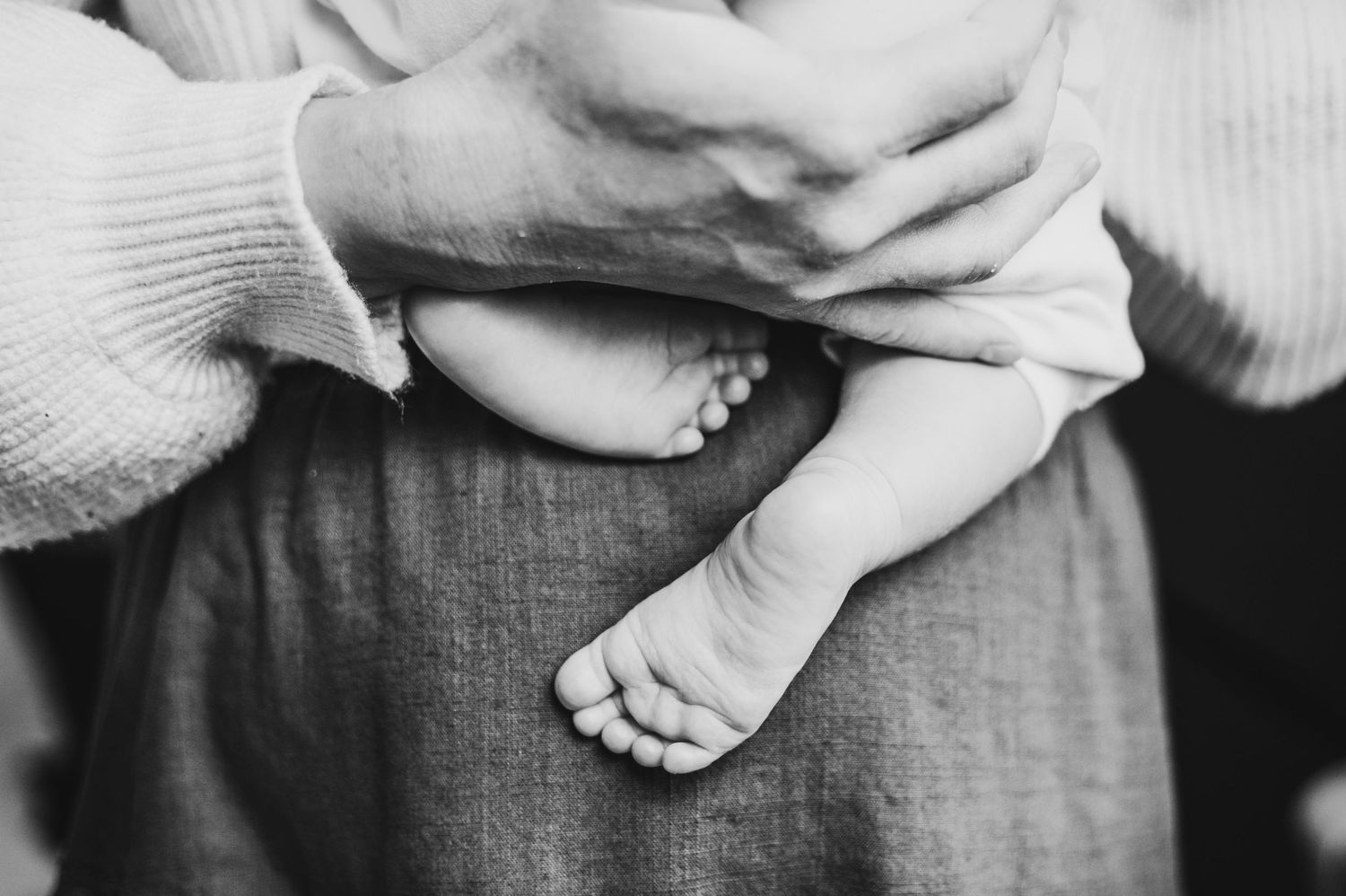 Mississauga newborn photographer captures a mother holding her newborn baby and his bare feet hang down against her.