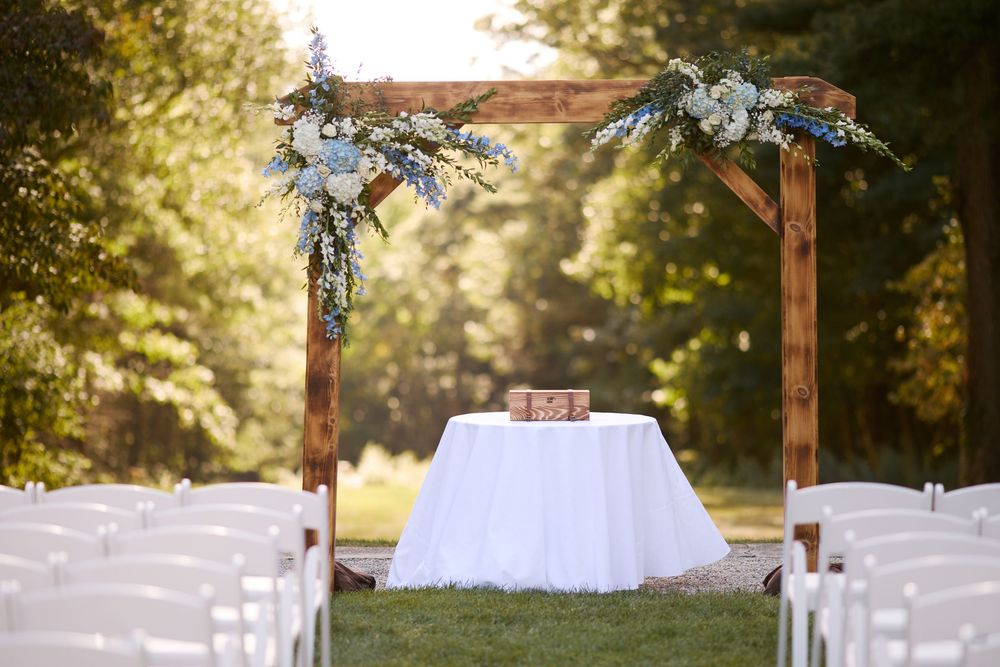 Garden wedding ceremony setup with wooden arch adorned with white flowers, white chairs, and draped table at the Bradley Estate.