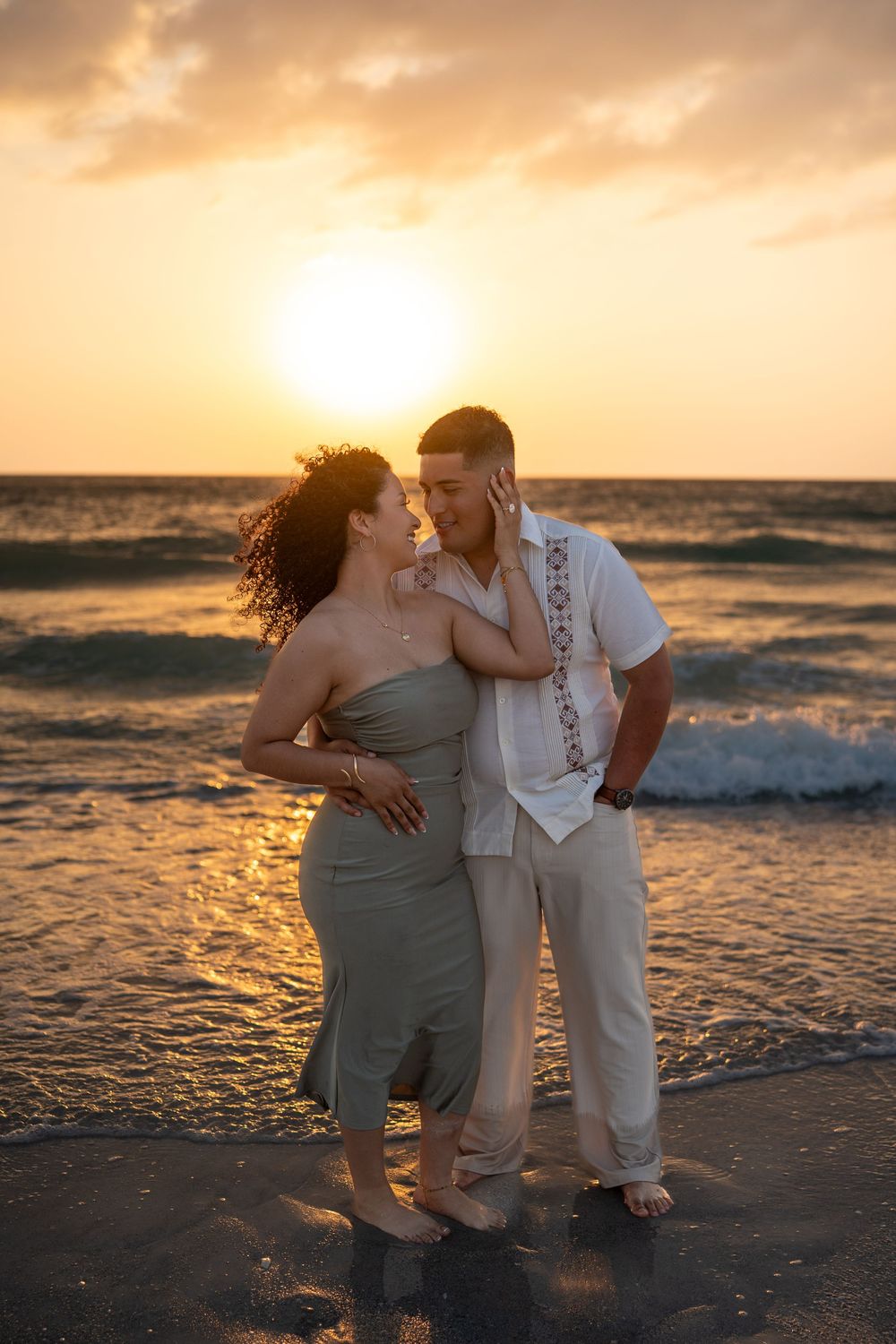 Couple sharing a romantic moment on the beach at golden sunset, waves crashing behind them.