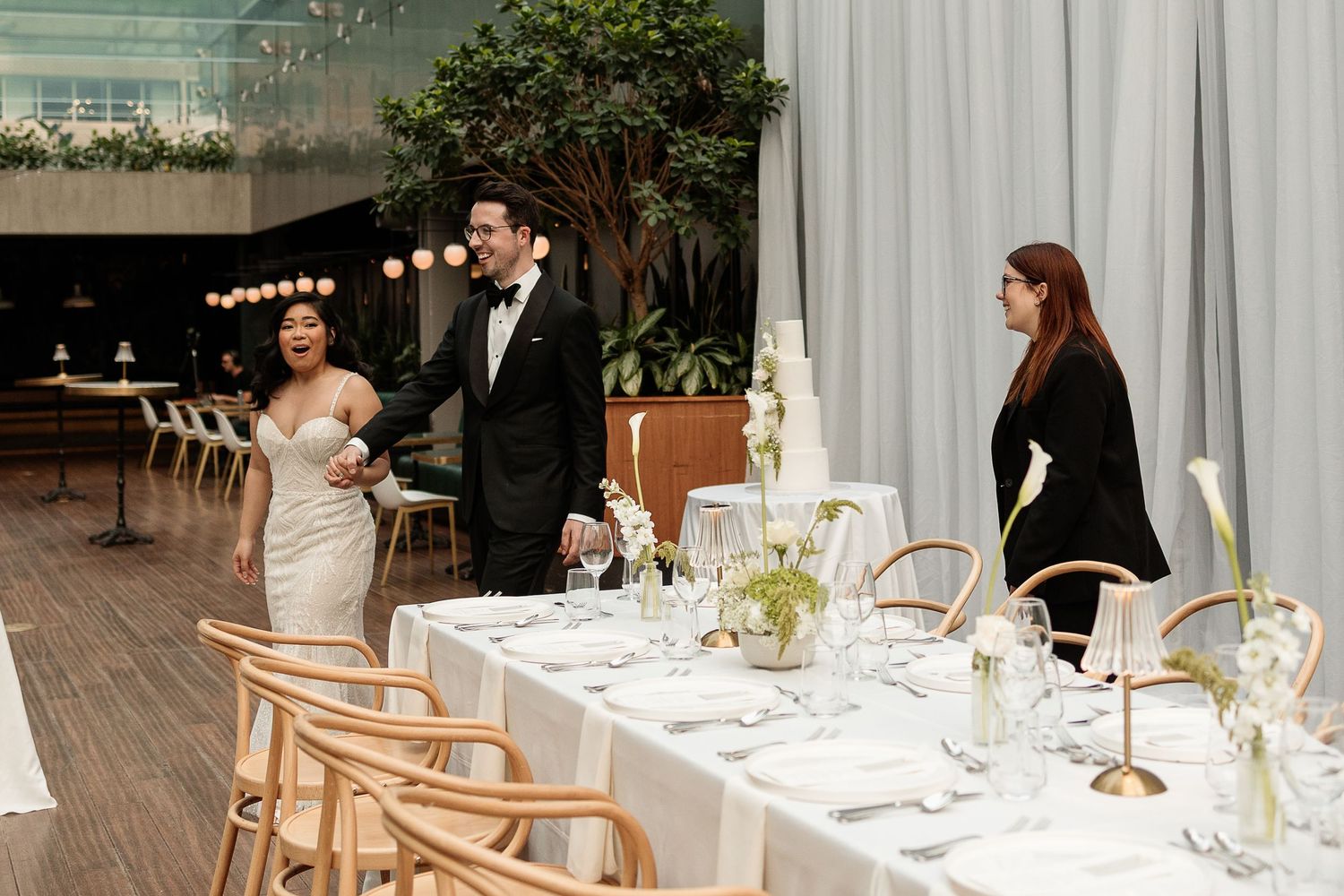 Elegant wedding reception room reveal with couple observing long white-tablecloth dining table with floral centerpieces at Le Cathcart.