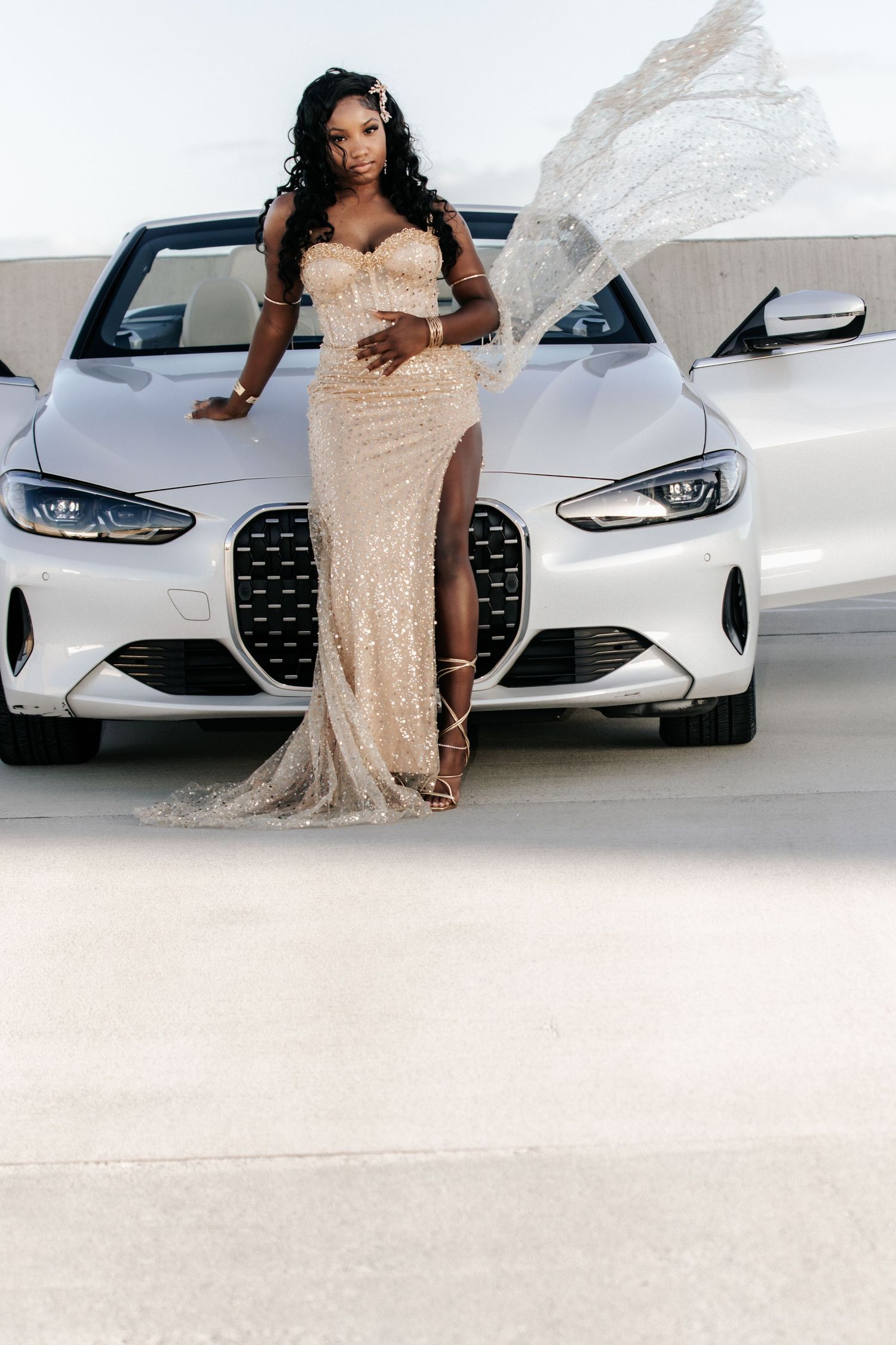 A woman in a sparkling beige sequined gown with a thigh-high slit poses gracefully against stone rocks outdoors.