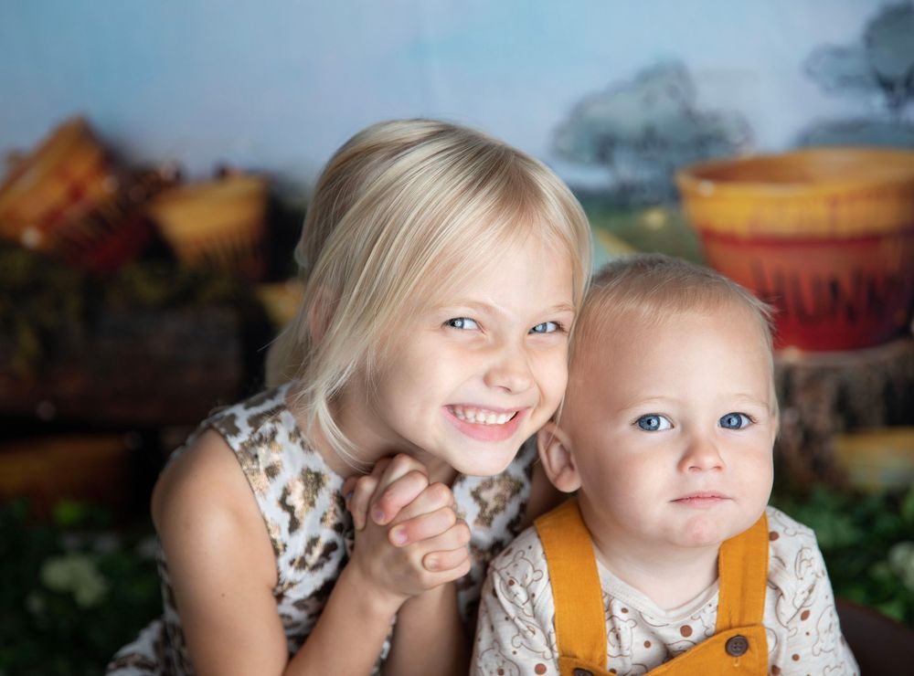 Two young siblings, a blonde girl and baby boy with blue eyes, pose together for a professional portrait photo.