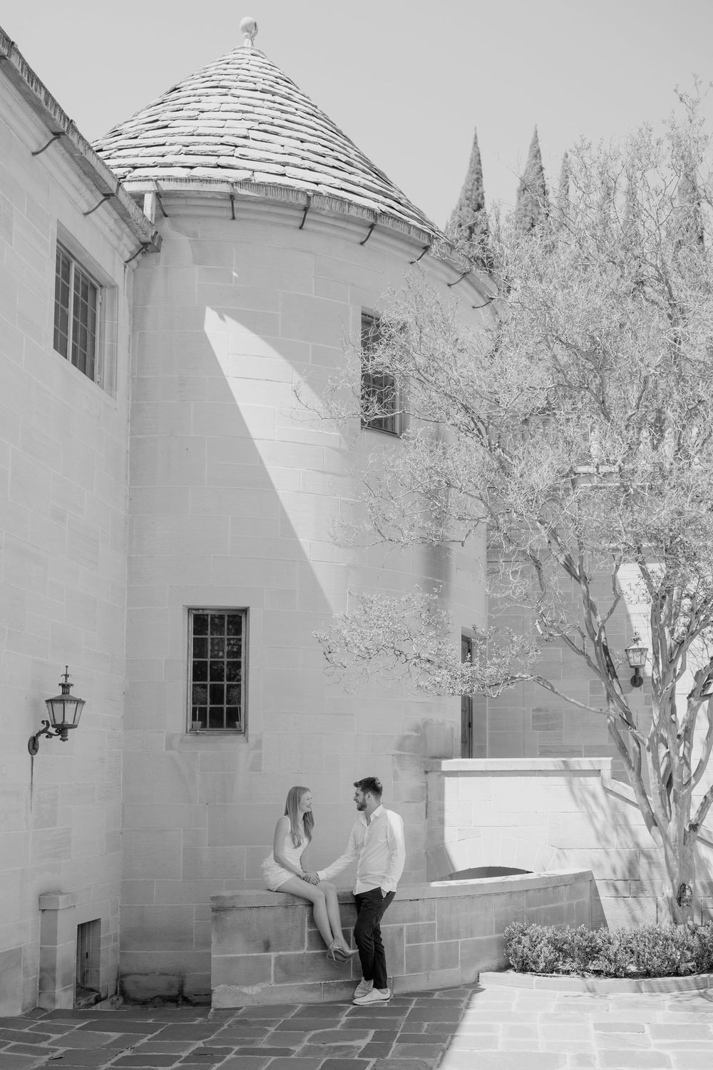 Couple sitting together by a stone castle turret building on a sunny day during an outdoor engagement session.