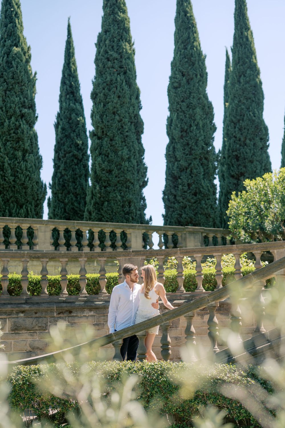 Couple sharing a romantic moment on stone balustrade steps surrounded by Italian cypress trees in a formal garden.