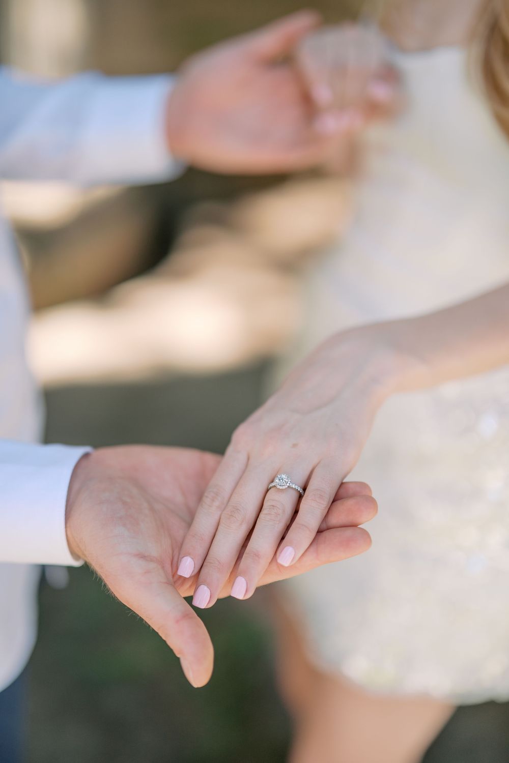Bride and groom holding hands showing diamond engagement ring with pink manicure at wedding ceremony.