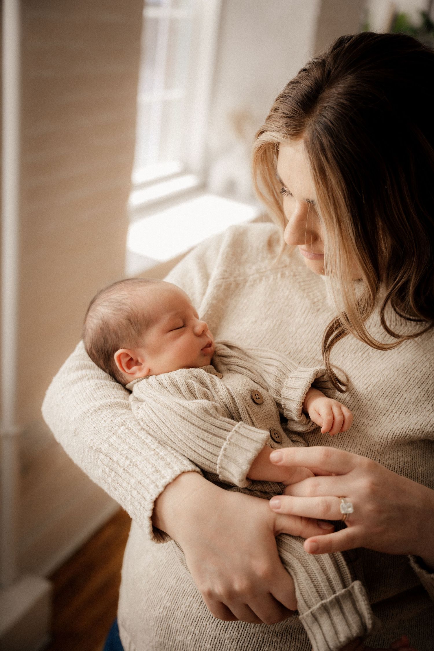 Newborn baby sleeping peacefully in an adult hand, wearing a cozy beige knit sweater.