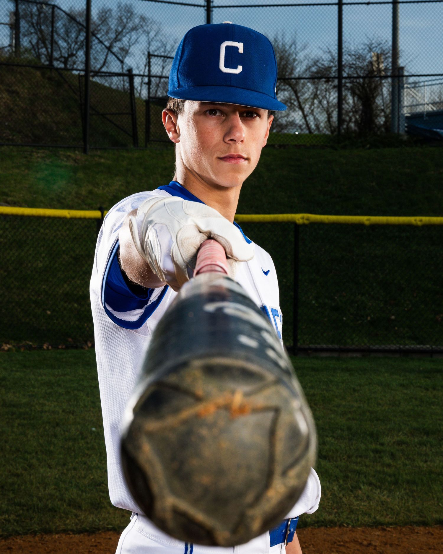 Young baseball player in blue uniform and cap pointing glove toward camera on outdoor field.