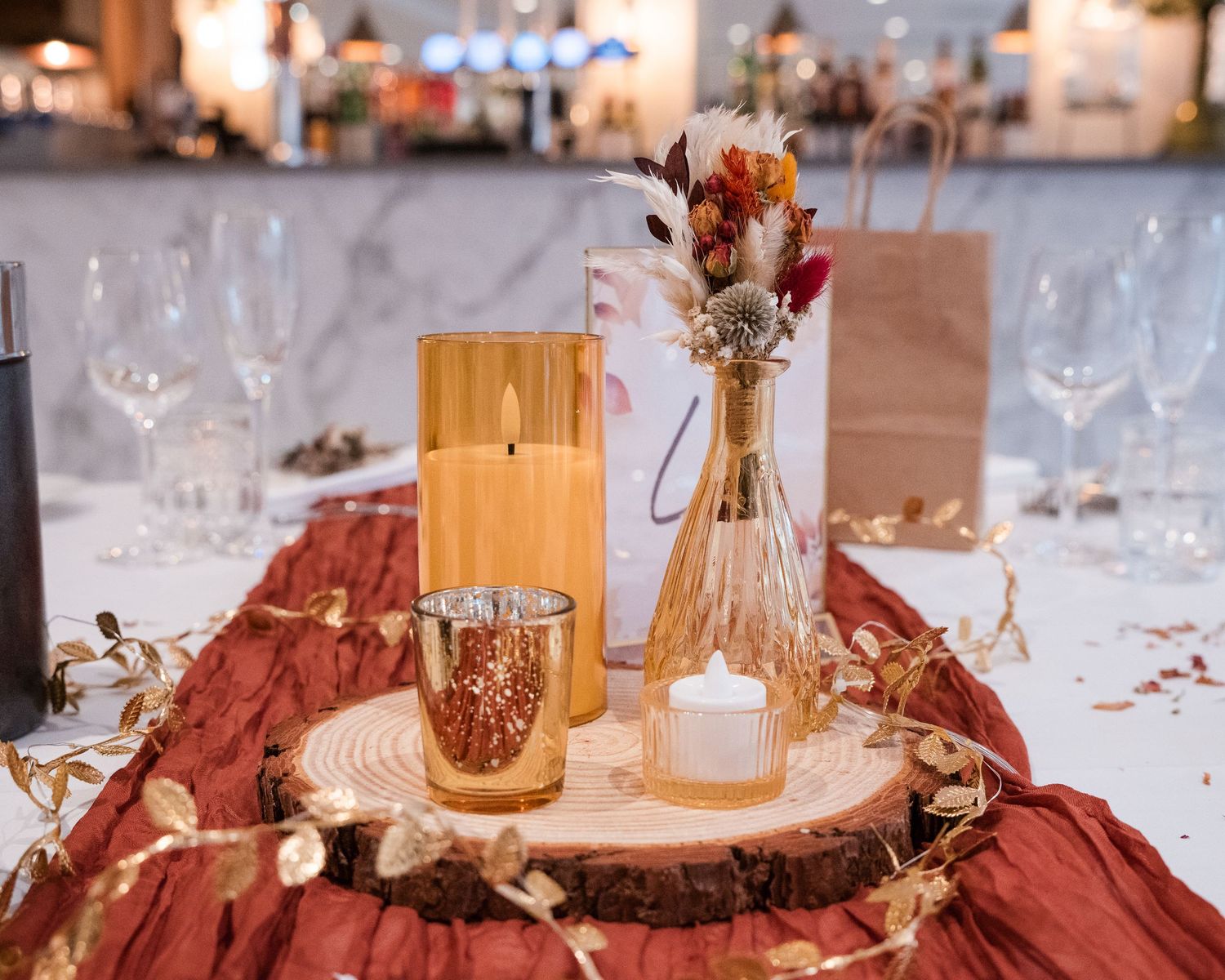 Elegant autumn wedding table centerpiece with candles, dried flowers, and rustic wood slice.