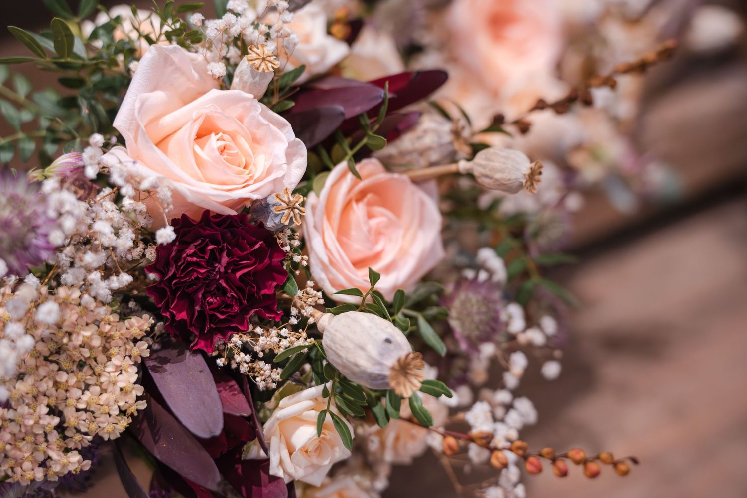 Close-up of romantic wedding bouquet featuring peach roses, burgundy carnations, and baby's breath.