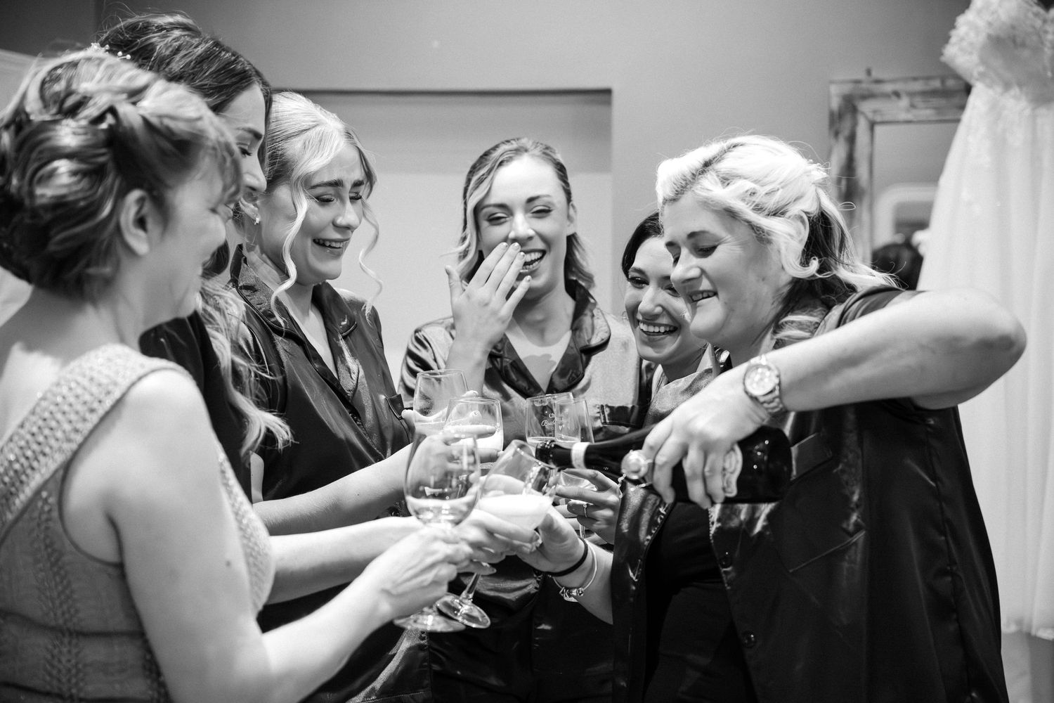 Black and white photo of bridesmaids laughing and toasting champagne glasses during bridal party getting ready celebration.