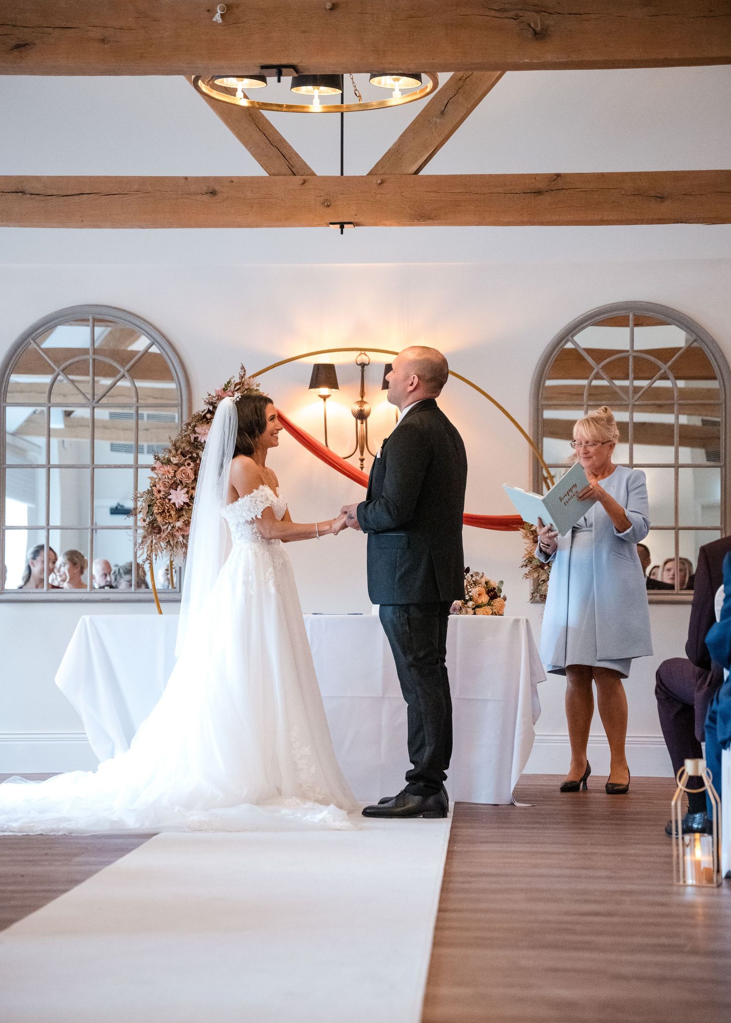 Bride and groom exchange vows at a rustic wedding ceremony venue with wooden beams and arched mirrors.