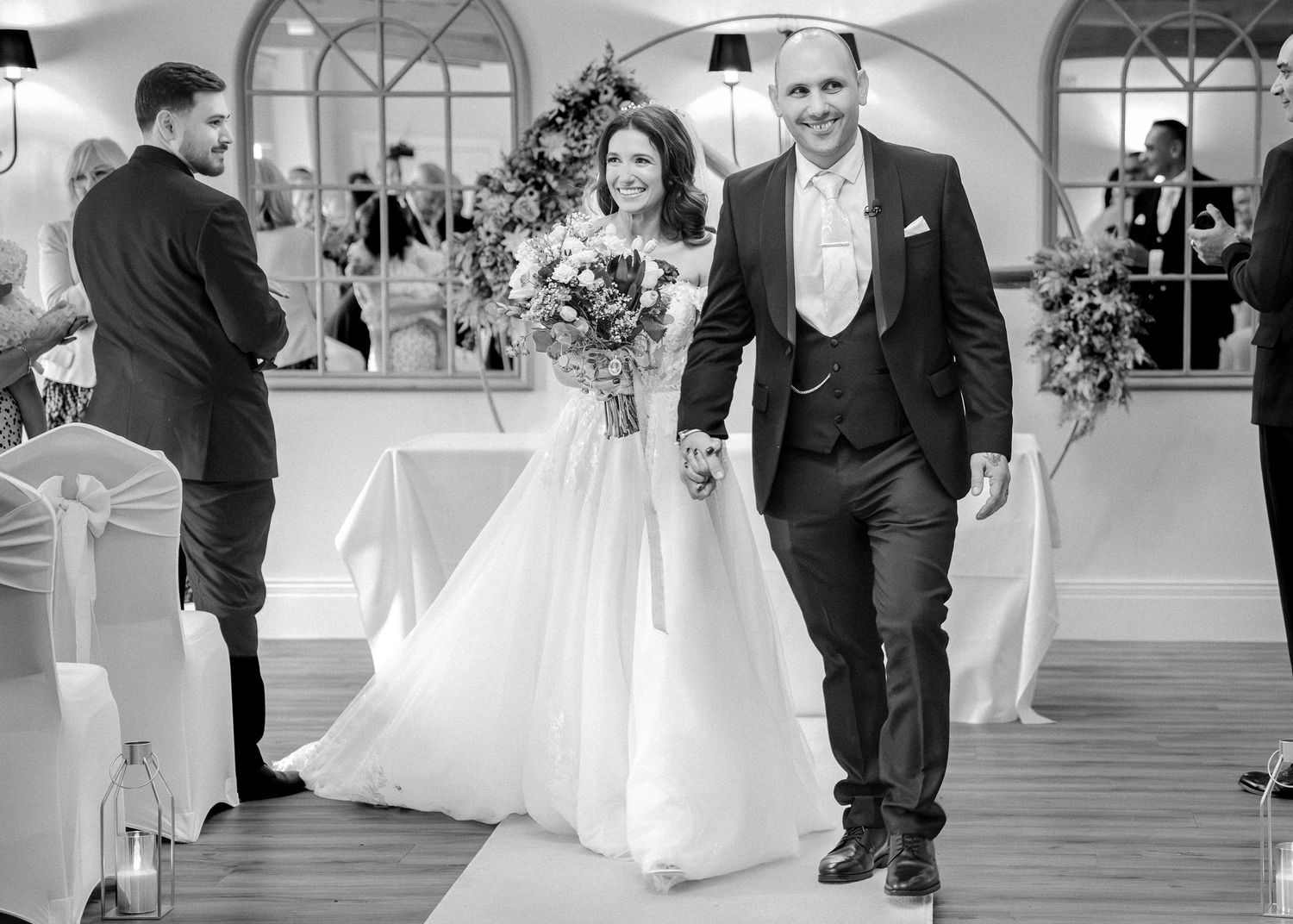 Newlyweds walk hand in hand down the aisle in a black and white photo after their wedding ceremony.