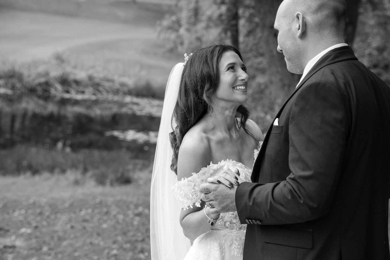 Black and white photo of glowing bride laughing while holding hands with groom outdoors.