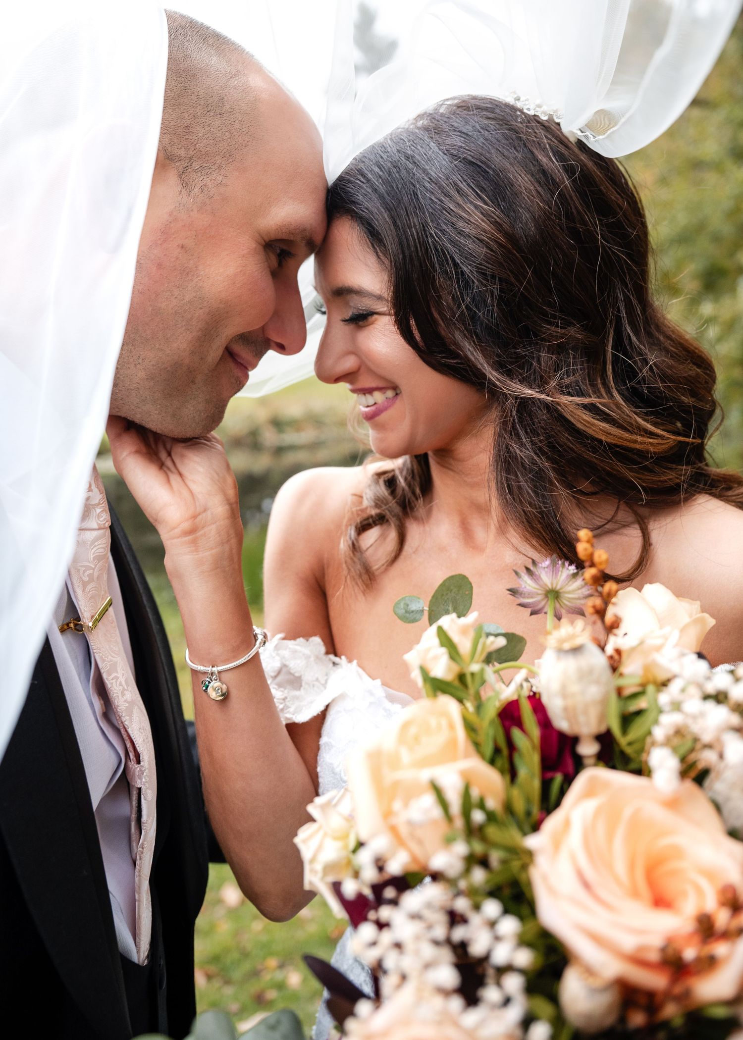 Bride and groom touching foreheads intimately, bride holding a lush floral bouquet.