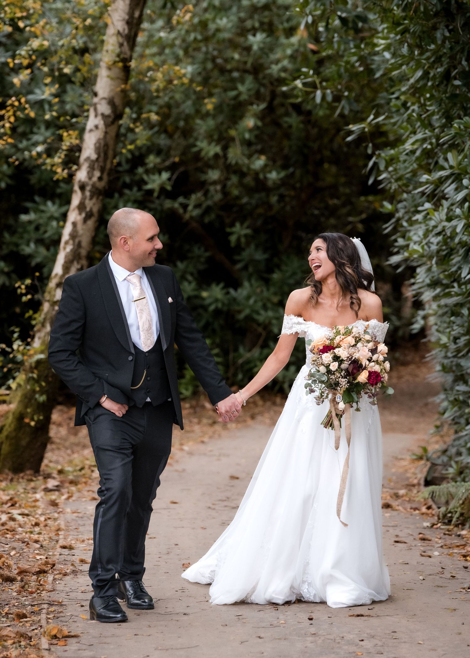 Bride and groom laughing joyfully while walking hand in hand through an autumn garden.