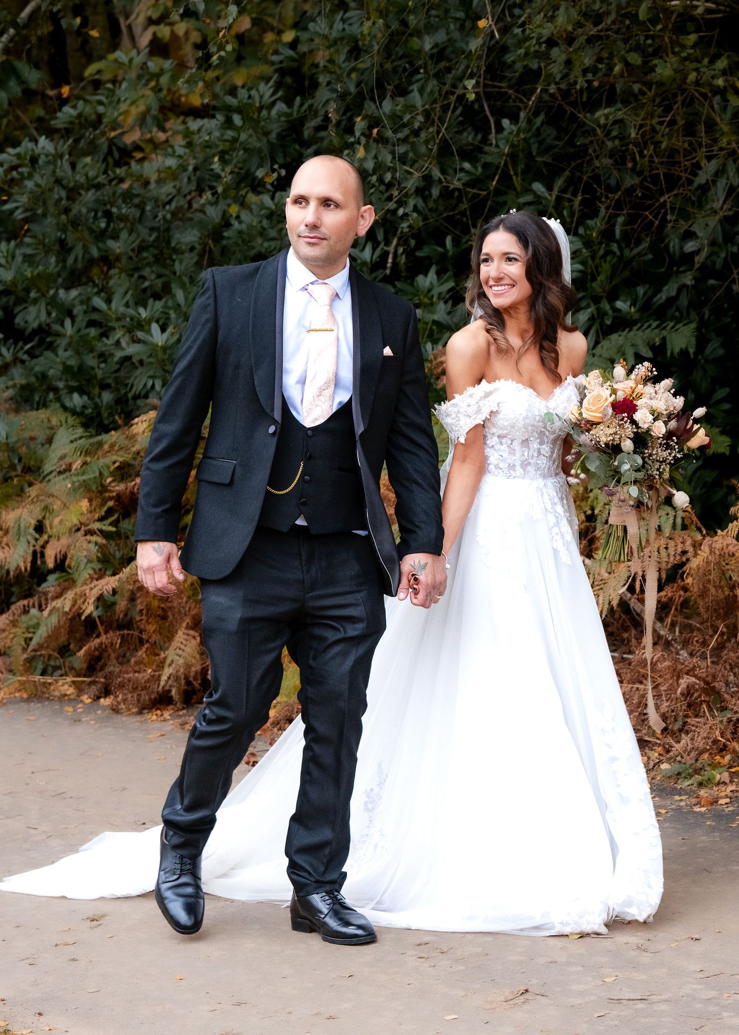 Bride in white off-shoulder gown and groom in black suit walking together outdoors.