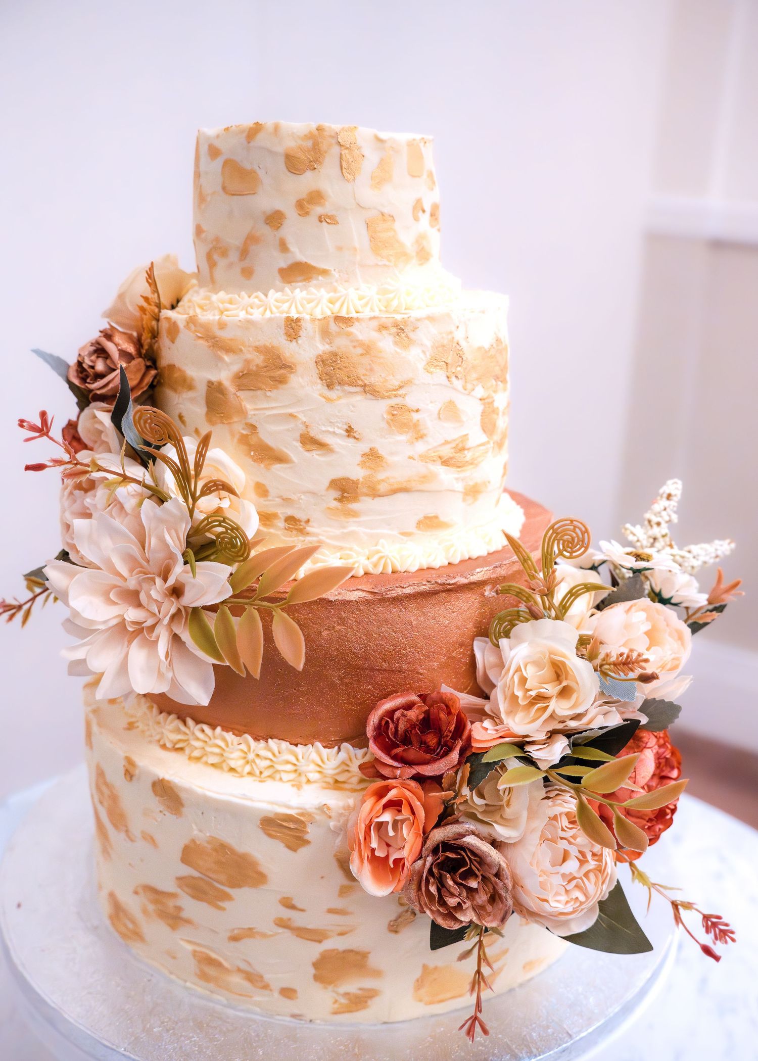 Elegant three-tier wedding cake with gold accents and colorful floral decorations.