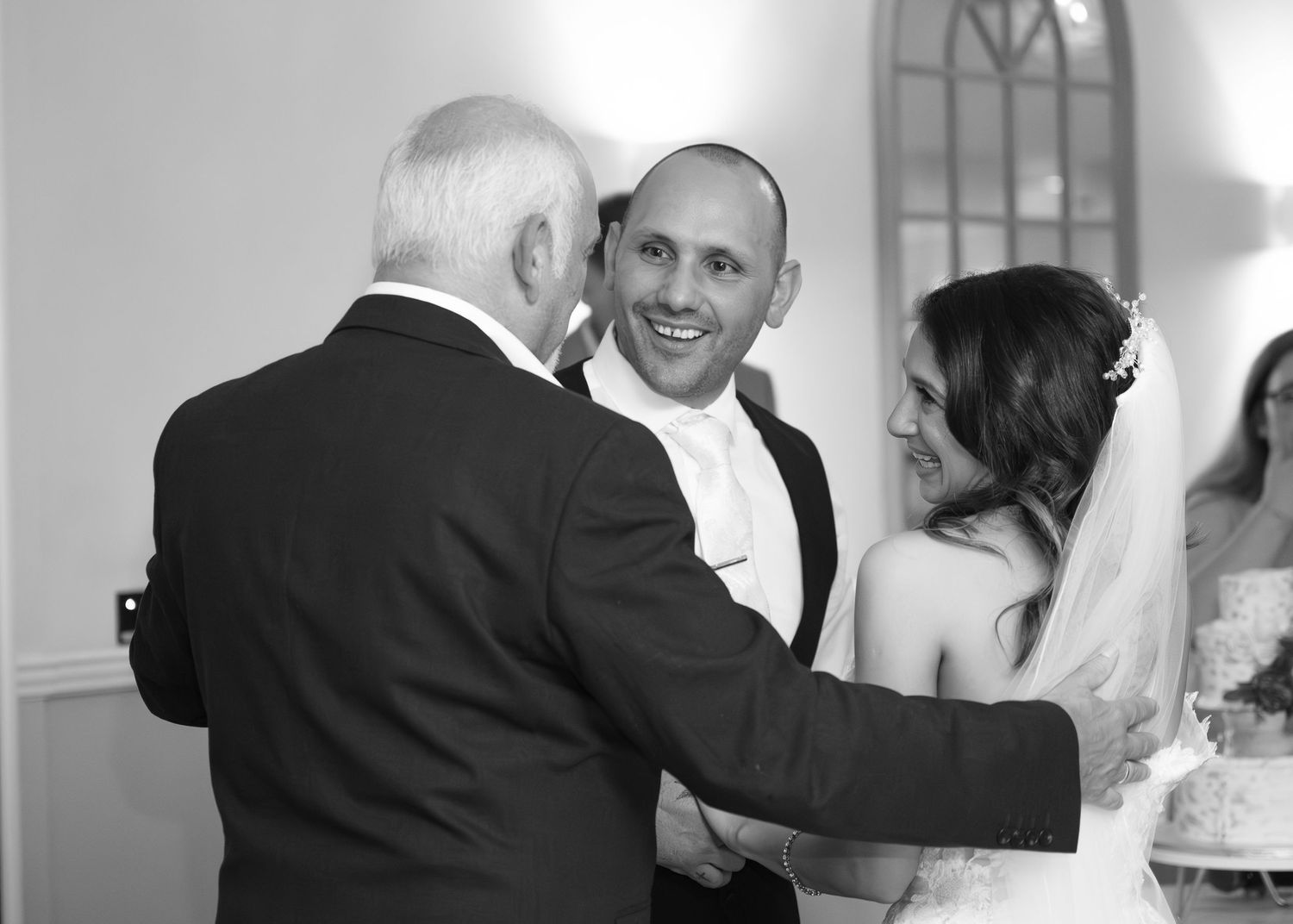 Black and white photo of smiling groom greeting an elderly guest at wedding ceremony.