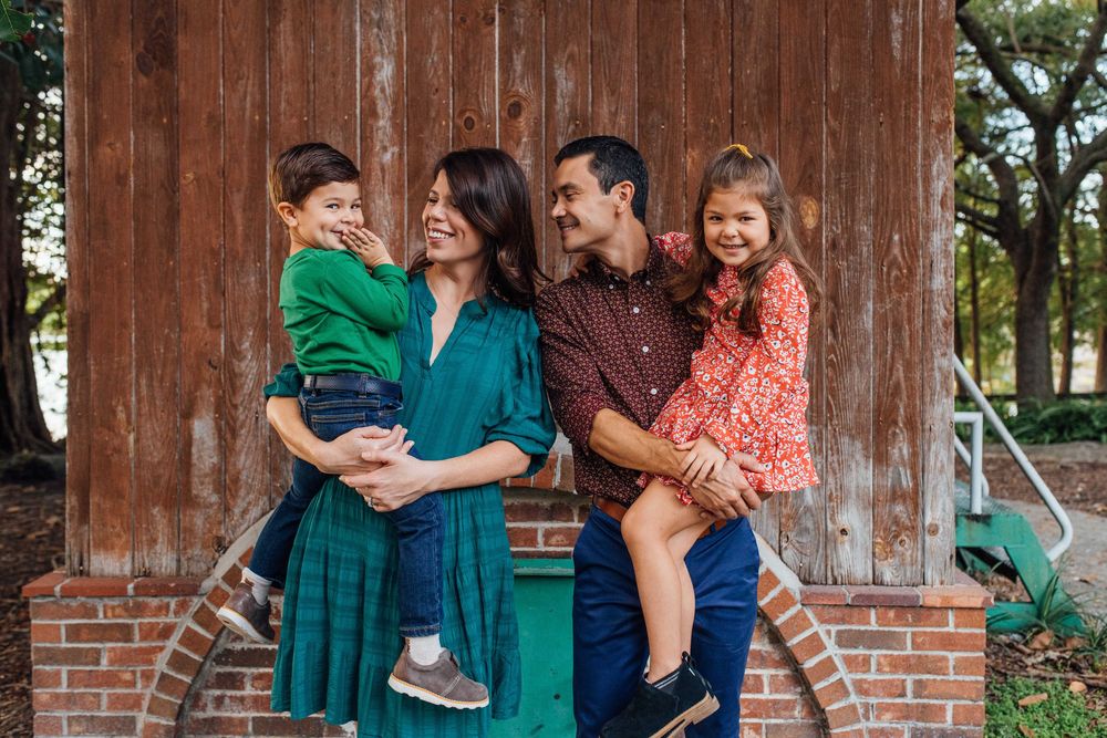 Joyful family of four laughing together outdoors beside a rustic wooden barn building.