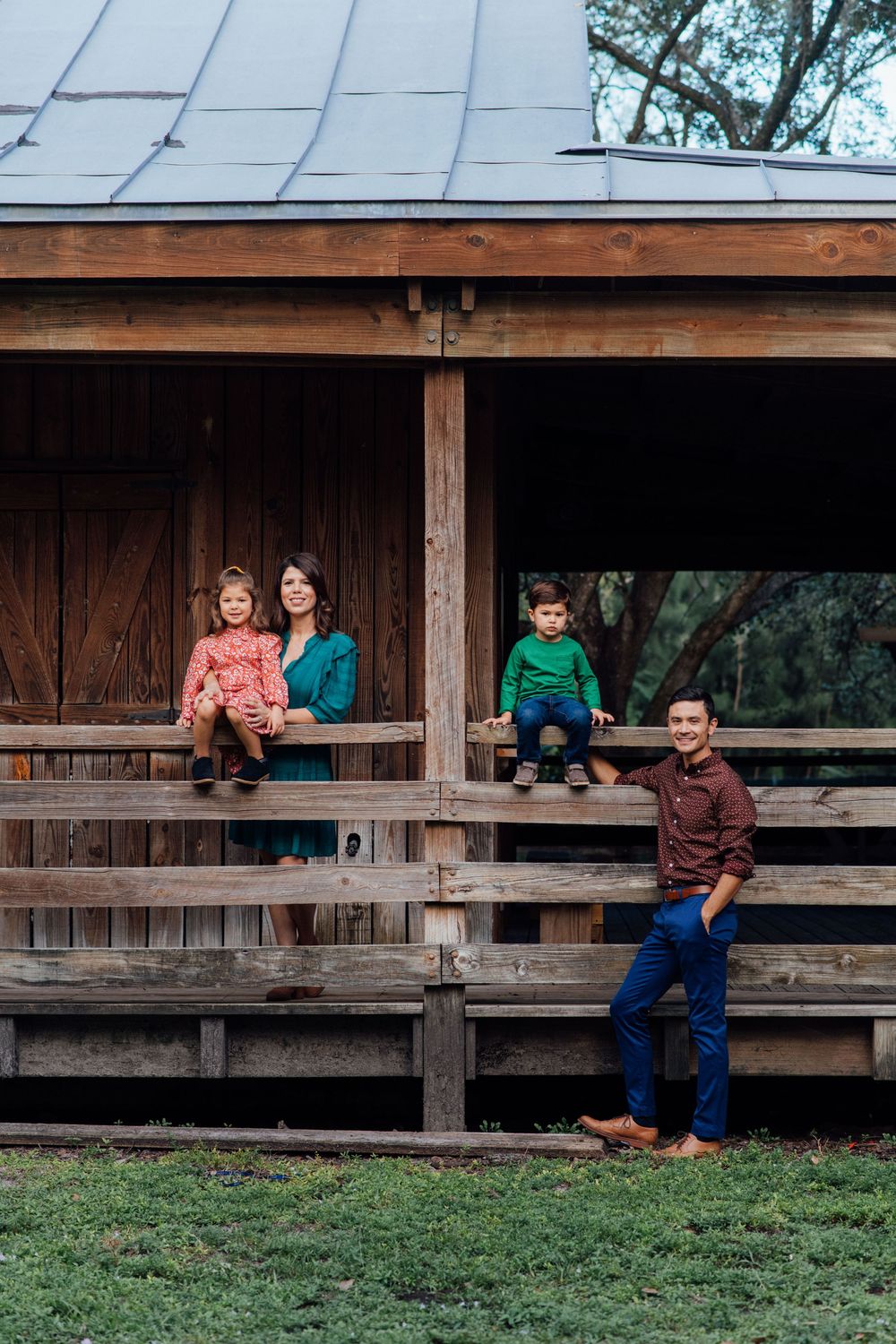 Happy family posing on wooden porch of rustic cabin with two children and parents in colorful outfits.