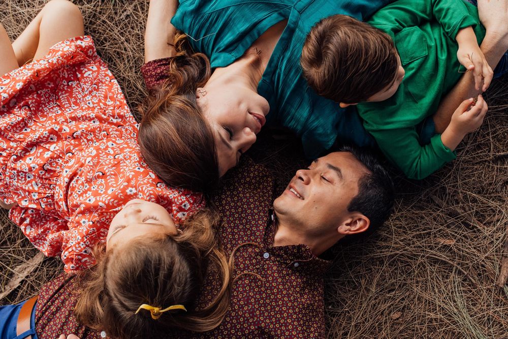 Family of four lying on dry grass looking at each other in a candid overhead portrait.