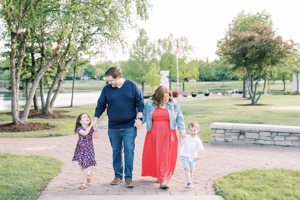 Happy family of four walking together on a park pathway at golden hour.