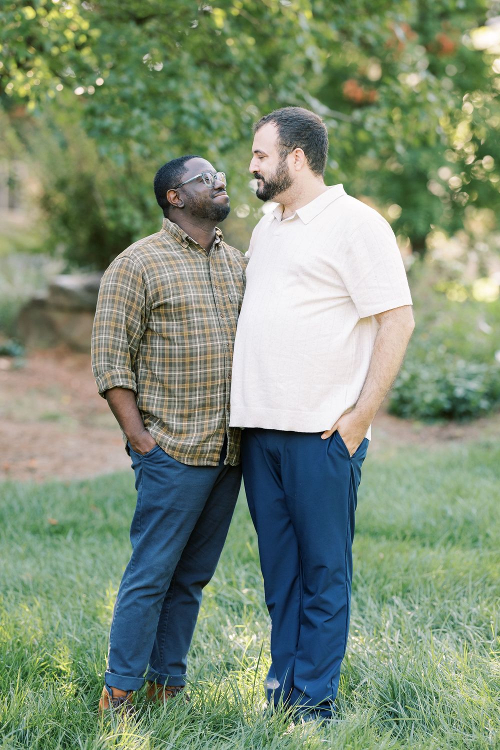 Two men sharing a joyful moment outdoors, standing on green grass with lush trees in the background.