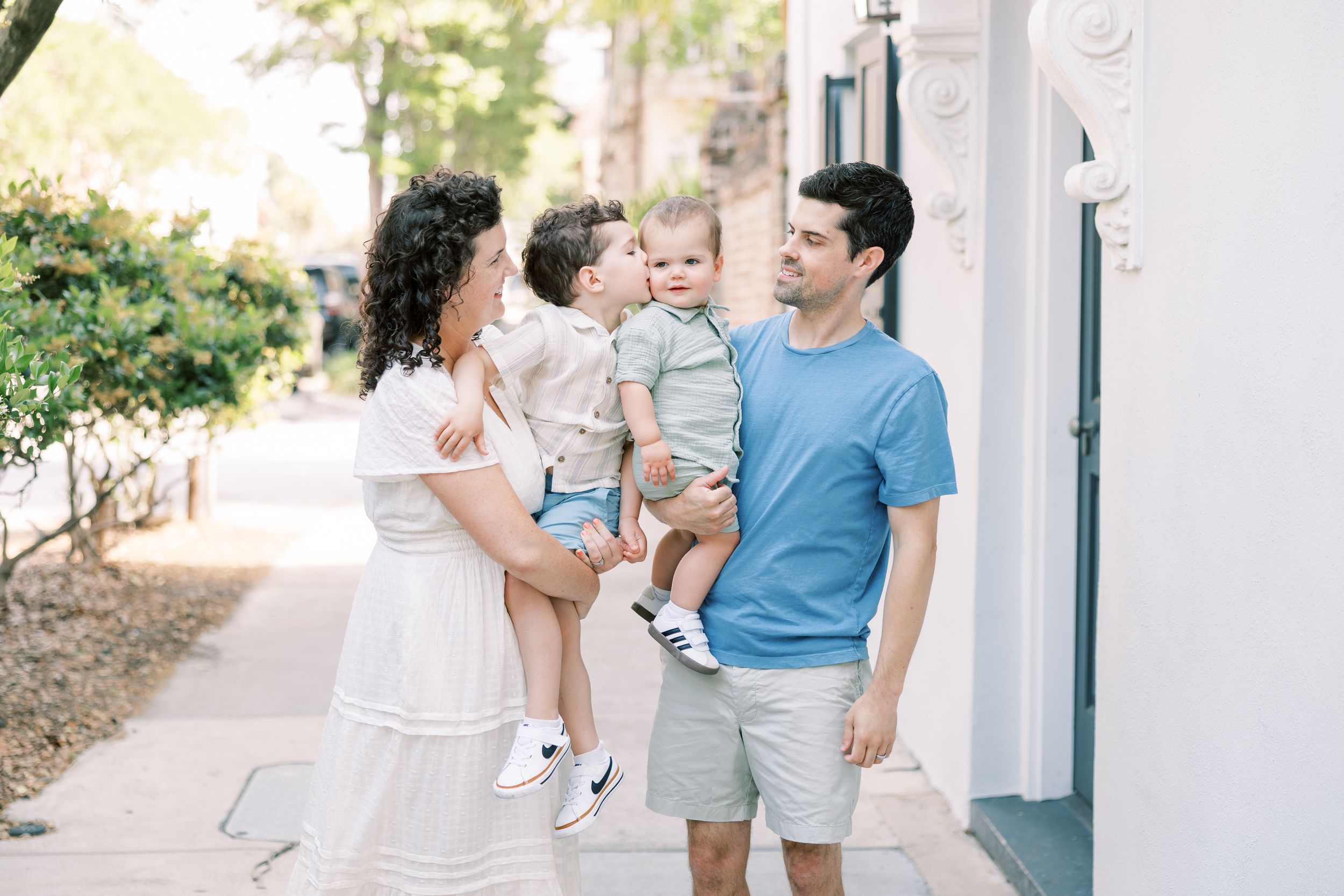 Happy family with two toddlers enjoying a sunny day on a charming tree-lined sidewalk.