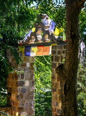 Stone gate adorned with colorful Tibetan Buddhist prayer flags surrounded by tropical trees.