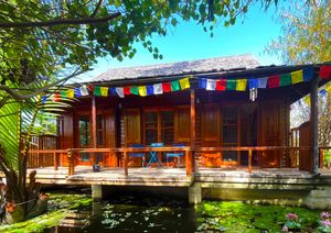 Wooden pavilion over a koi pond with colorful Tibetan prayer flags and lush greenery in a serene garden setting.