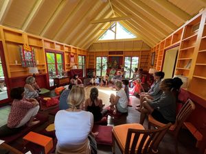 Group of people sitting in a circle inside a wooden meditation hall with orange walls and high vaulted ceiling.