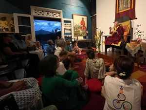 Buddhist monk teaching a meditation class to seated students in a serene, decorated room with mountain views.