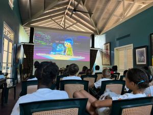 Children watching Inside Out on a large projection screen in a tropical venue with wicker chairs.