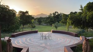 Circular stone patio with table and chairs overlooking lush green golf course at sunset with mountain views.