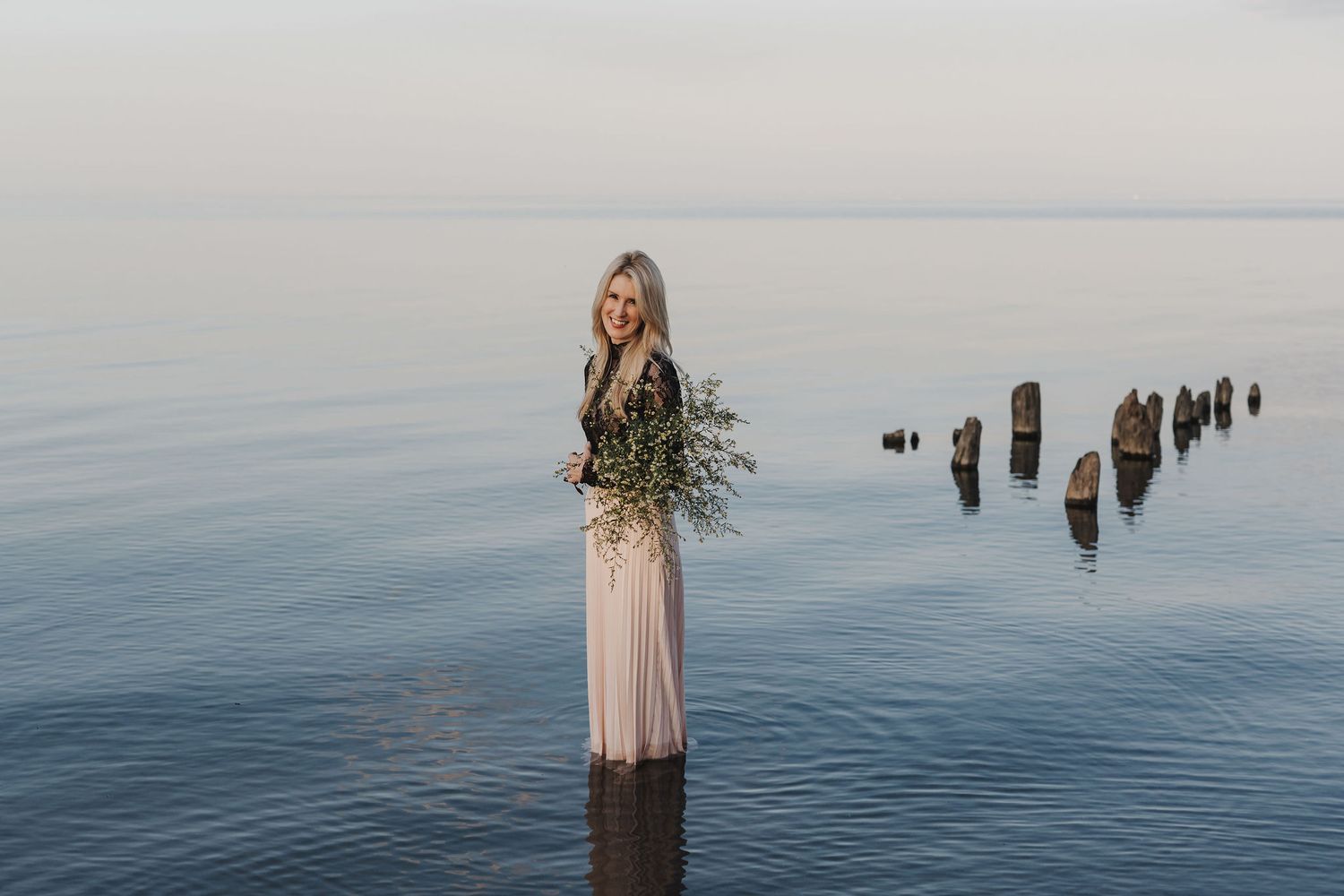 Michelle Hugill standing in calm lake water, holding a bouquet of wildflowers