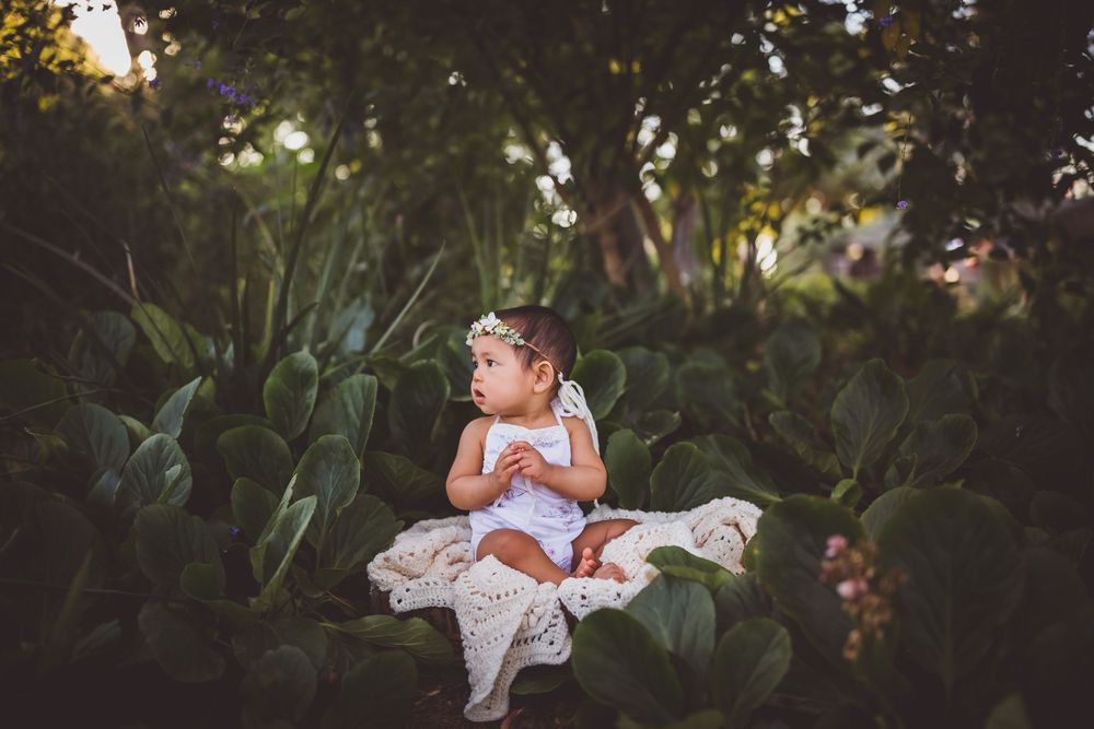 A toddler girl in a white dress sits on a lace blanket during her photo shoot with family photographer heidi grace photography
