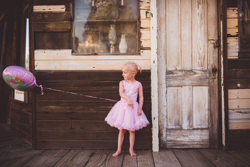 Young girl in pink tutu dress holds balloon on rustic wooden porch of weathered building in beaumont ca