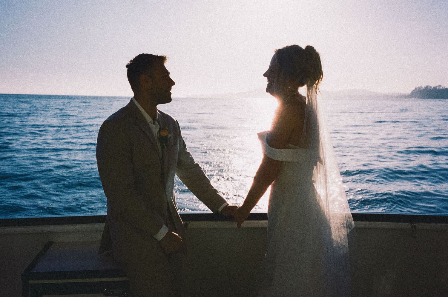 Bride and groom holding hands on a boat at sunset with ocean backdrop on their wedding day.